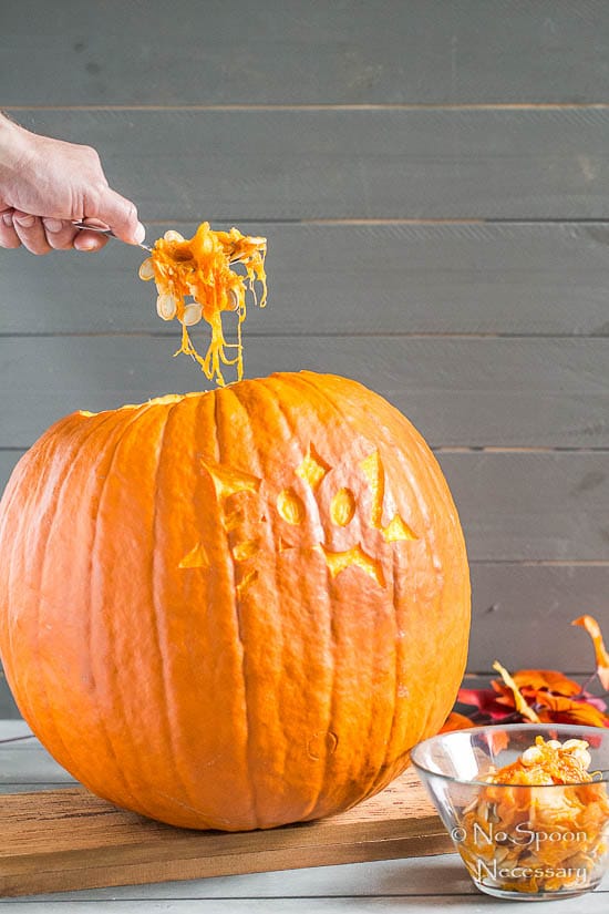 Straight on shot of a person holding a spoon and removing the pumpkin seeds from a pumpkin - photo of the third step of How To Make A Pumpkin Keg.
