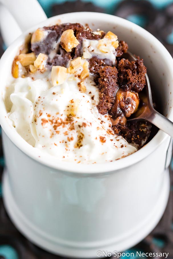 Angled up close shot of a spoon digging into a Snickers Lava Mug cake with whipped cream and chopped peanuts