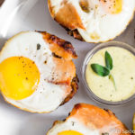 Overhead shot of a Turkey, Egg & Stuffing Muffin on a white plate with a small, clear bowl of blender sage hollandaise sauce and other muffins slightly out of frame