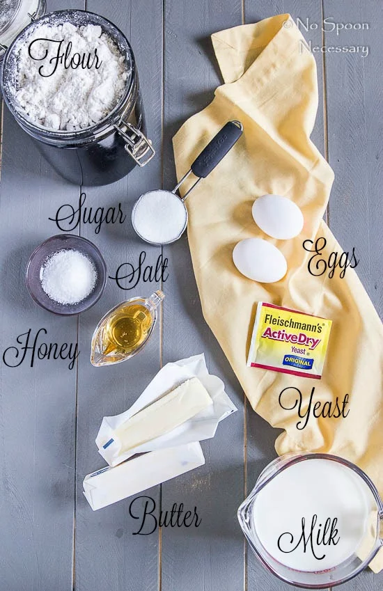 Overhead shot of all the ingredients needed to make Honey & Brown Butter Parker House Rolls neatly organized on a gray wooden surface with the names of each ingredient written out.