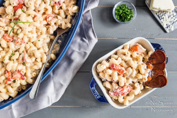 Overhead shot of Truffle Lobster Macaroni n' Cheese in a large blue baking dish and a smaller, individual baking dish with a ramekin of chives and a chunk of parmesan in the corner.