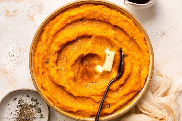 Overhead photo of butternut squash mash with a pat of butter in a white serving bowl.