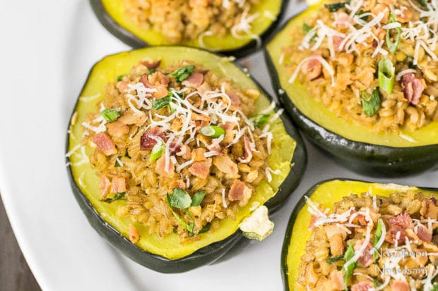 Overhead, landscape shot of Bacon Scallion Farro Stuffed Acorn Squash garnished with sliced scallions and parmesan cheese on a white platter.