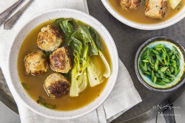 Overheat shot of a bowl of Ginger Chicken Meatball Miso Soup and Bok choy with a ramekin of sliced scallions, neutral linen and additional bowl of soup off to the side.