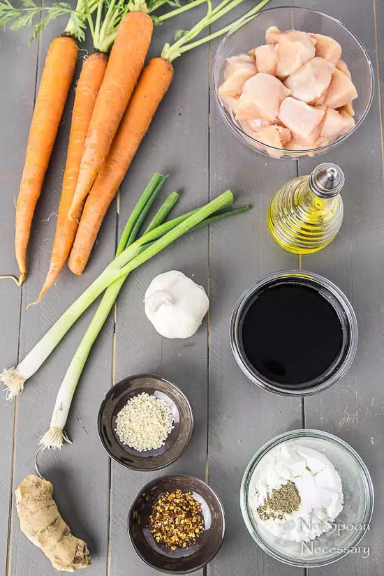Overhead shot of all the ingredients needed to make Honey Garlic Ginger Chicken Carrot Noodle Bowls neatly organized on a gray surface.