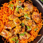 Overhead photo of stir fried honey garlic chicken breast with carrot noodles in a large black serving bowl.