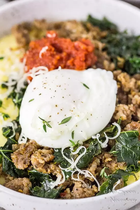 45 degree angle, up-close shot of a Sausage Breakfast Polenta Bowls with kale, sausage, poached egg and sundried tomato pesto with the focus on the poached egg.