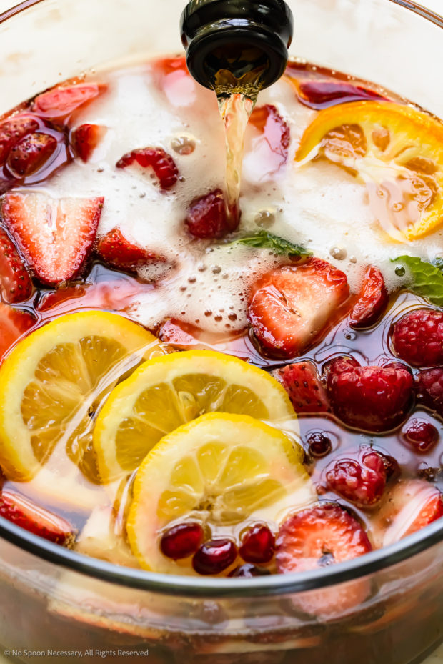 Close-up photo of champagne being poured into a pitcher of homemade sangria with strawberries.