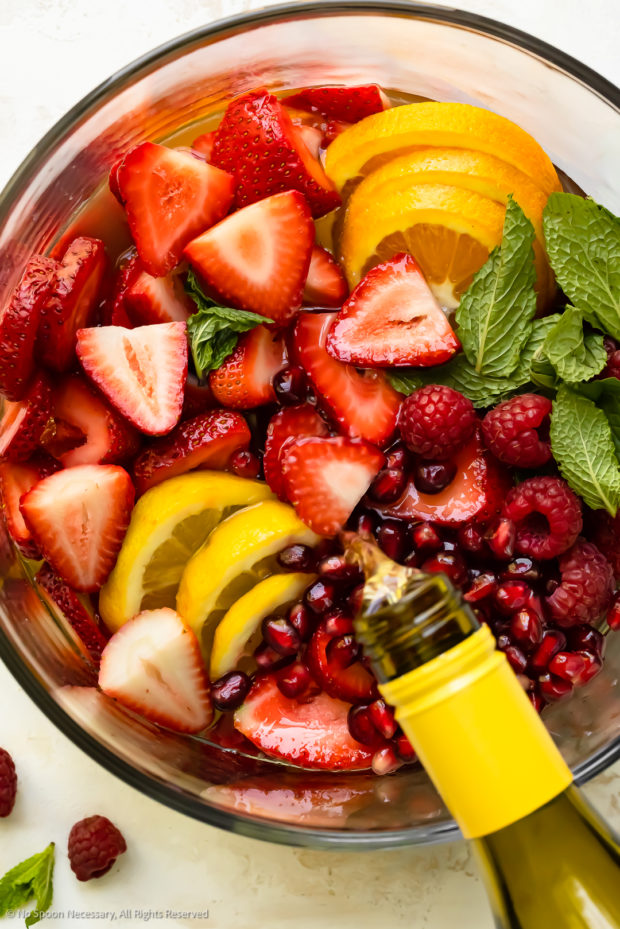 Overhead photo of a bottle of white wine being poured over sangria fruit in a serving bowl.