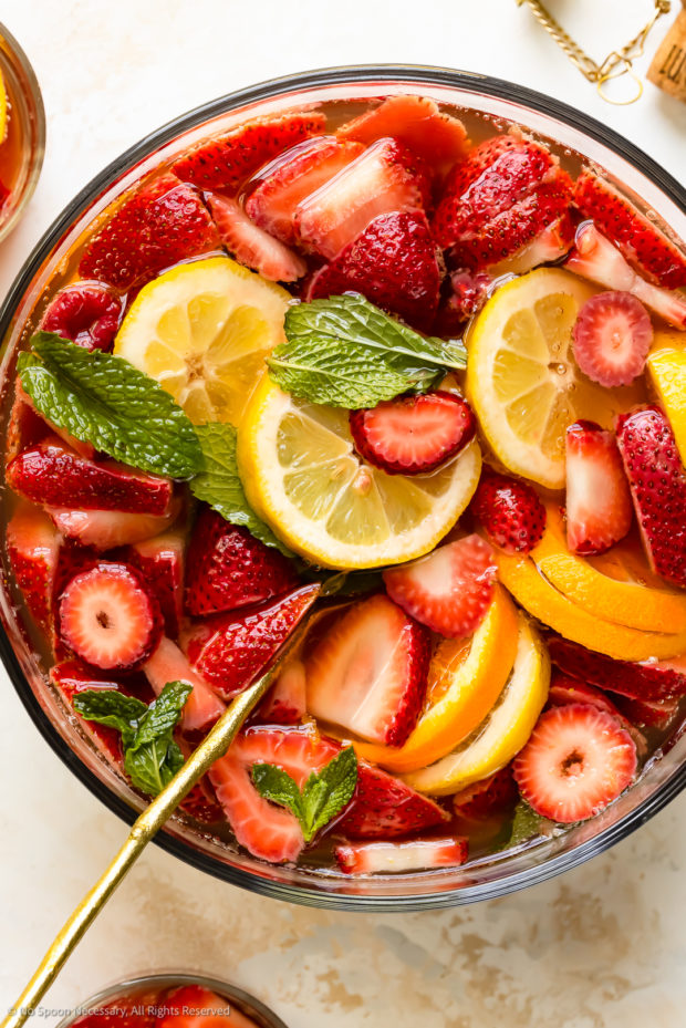 Overhead photo of strawberry white sangria in a large punch bowl with a cocktail spoon inserted into the sangria.