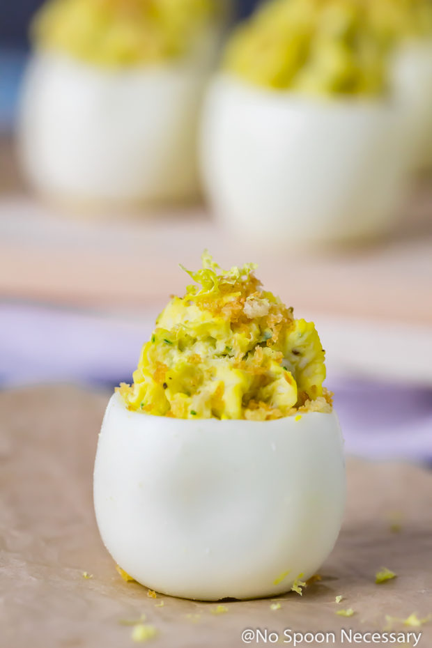 Straight on shot of a Crab Cake Deviled Egg with a wood board topped with more deviled eggs blurred in the background.