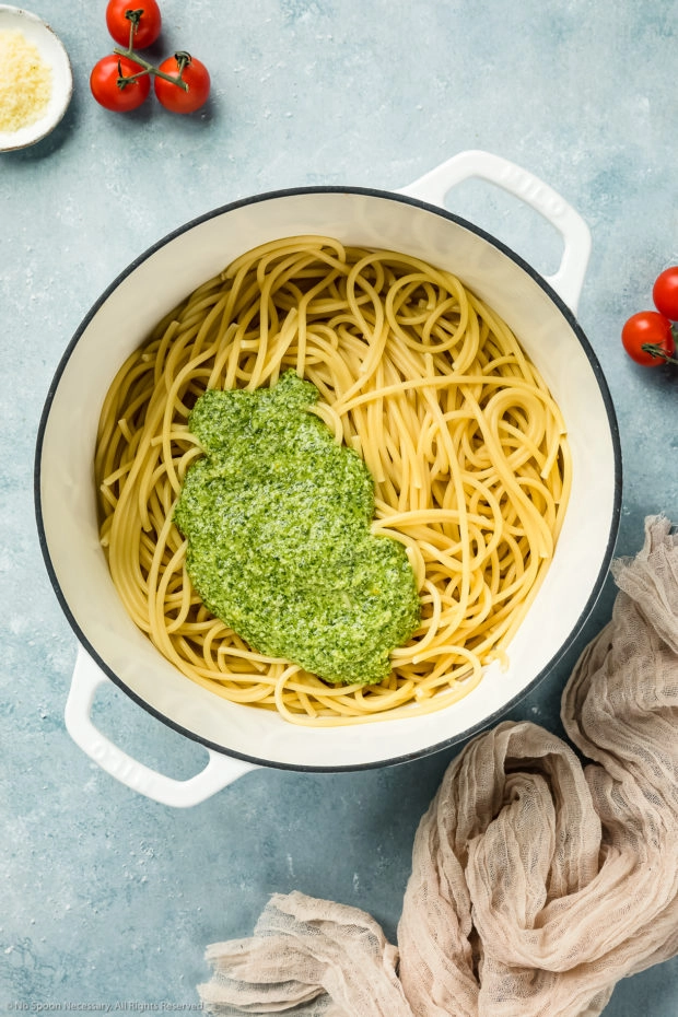 Overhead shot of a large white pot filled with al dente pasta and topped with a generous dollop of homemade arugula pesto - photo of step 4 of the arugula pesto pasta recipe.