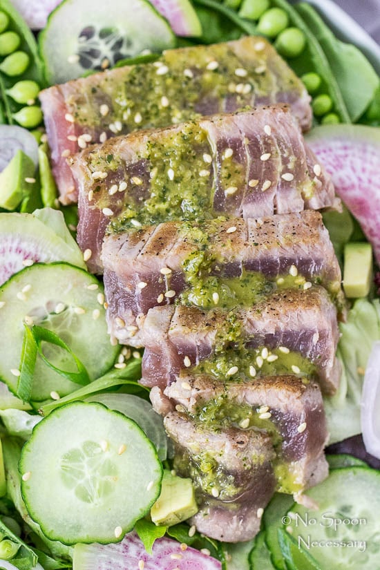 Overhead, up close shot of an Ahi Tuna Spring Salad drizzled with Asian vinaigrette, with the focus on the sliced tuna portion of the salad.