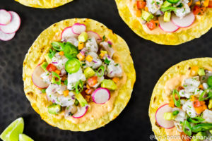 Overhead, landscape photo of Mexican Shrimp Ceviche Tostadas on a black platter with lime wedges, and sliced radishes.