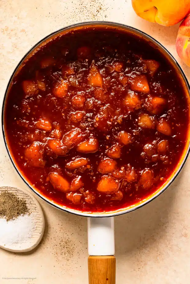 Overhead photo of a white saucepan with cooked fresh peaches in barbecue sauce.