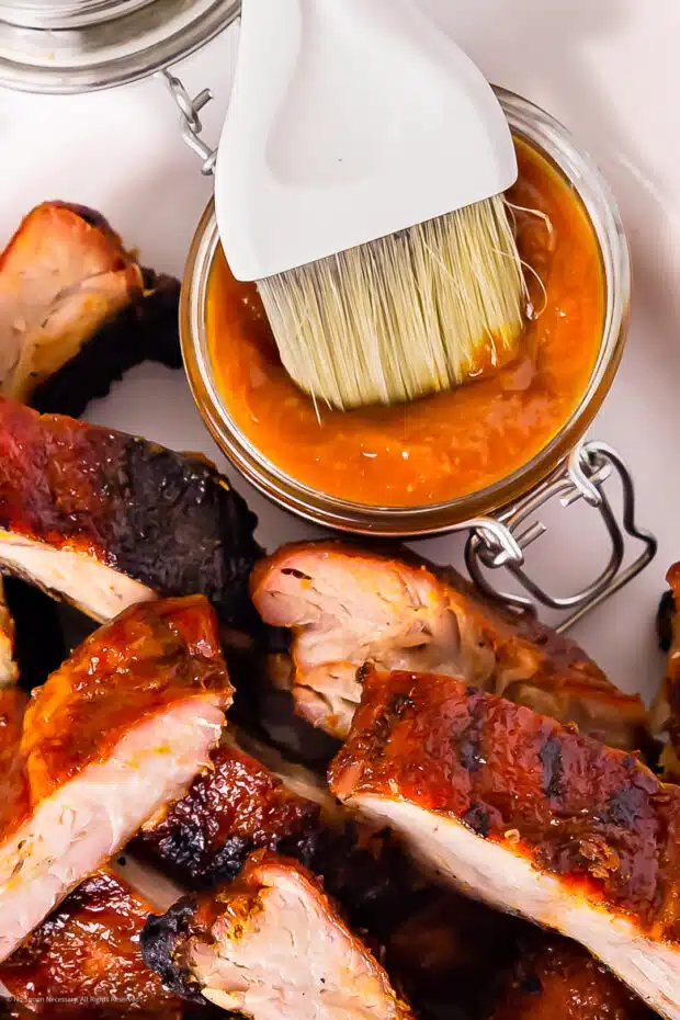 Overhead photo of a peach barbecue sauce in a glass storage container with peach glazed ribs next to the sauce.