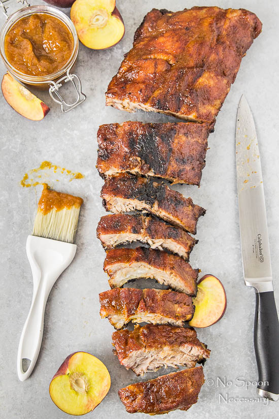 sliced baby back ribs surrounded by knife and basting brush with peach BBQ sauce