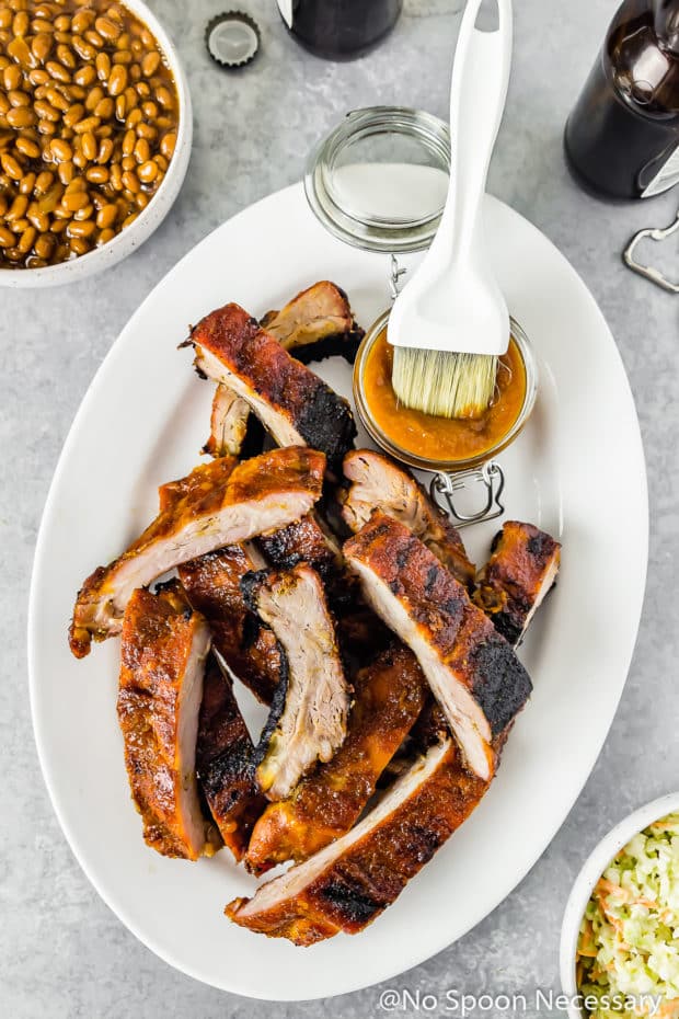 platter of grilled ribs with jar of Peach Sriracha BBQ Sauce surrounded by sides