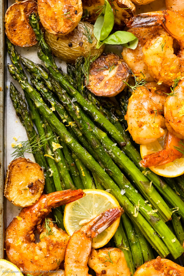 Overhead photo of roasted asparagus spears surrounded by potatoes and shrimp on a sheet pan