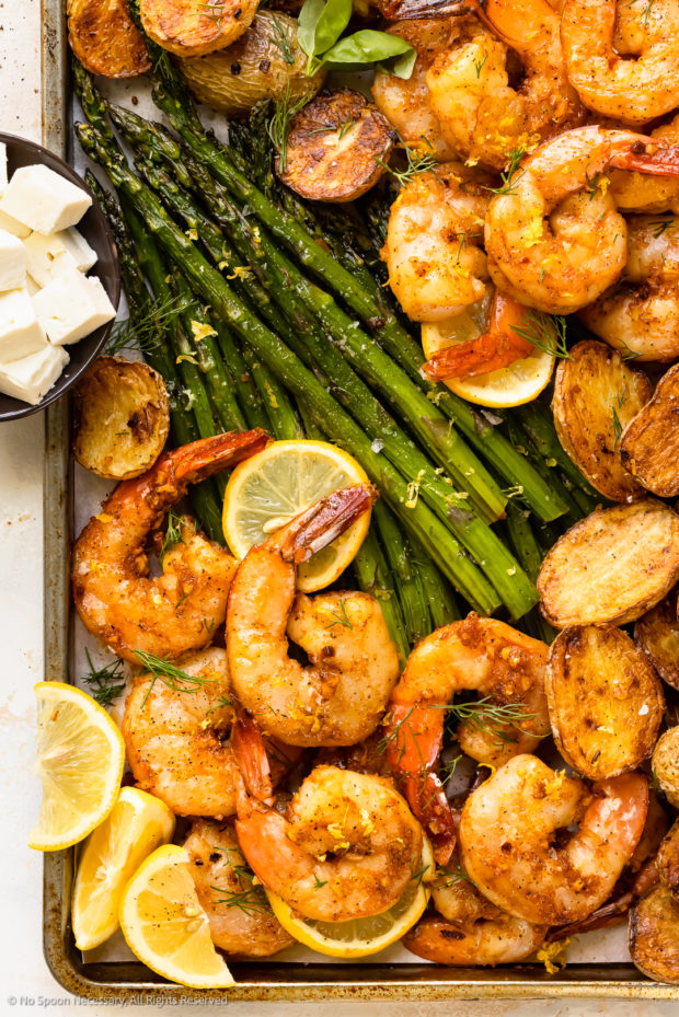 Overhead close-up photo of a shrimp potato bake with asparagus on a baking pan.