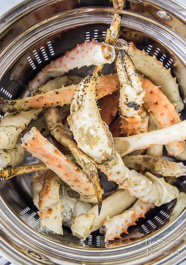 Overhead shot of king crab legs in a steamer basket - step one in the recipe to make Avocado, Mango & Crab Rolls.