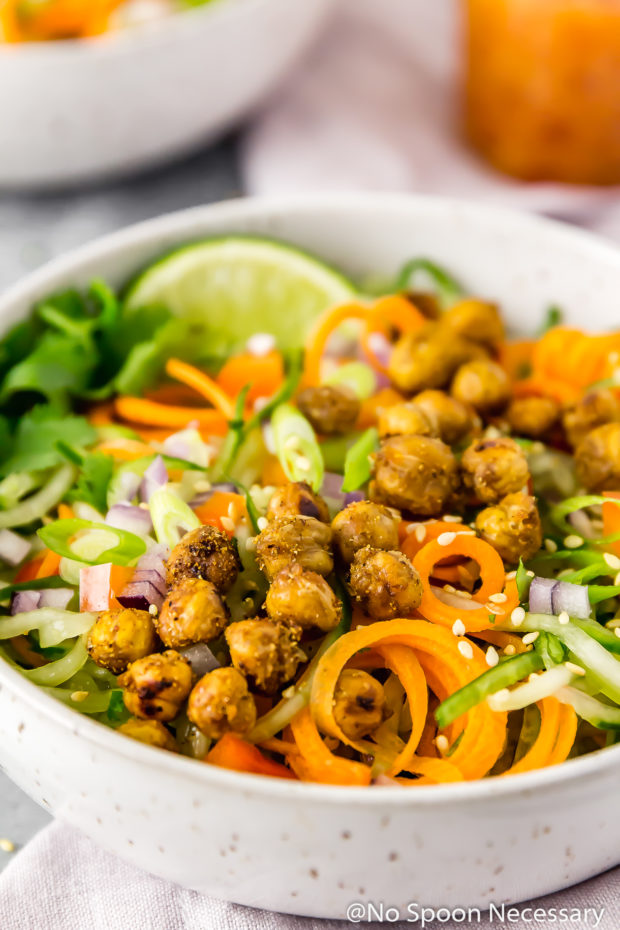 Angled shot of Thai Roasted Chickpeas with Vegetable Noodle Salad in a small bowl with an additional salad and jar of dressing barely visible in the background.