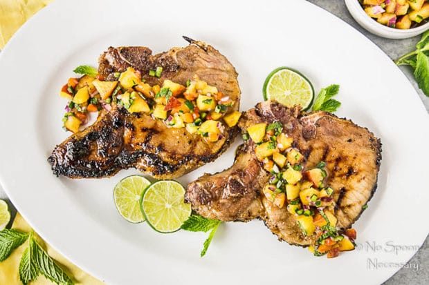 Overhead shot of Ginger Honey Glazed Pork Chops with Peach-Poblano Salsa on a white platter with slices of lime.