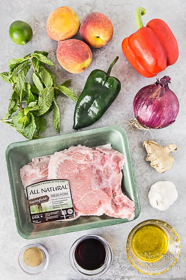 Overhead shot of all the ingredients necessary to make Ginger Honey Glazed Pork Chops with Peach-Poblano Salsa neatly organized on a light gray surface.