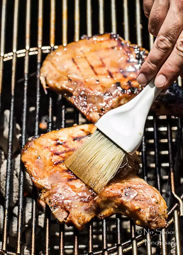 Slightly angled shot of Pork Chops on a grill being brushed with Ginger Honey Glaze.