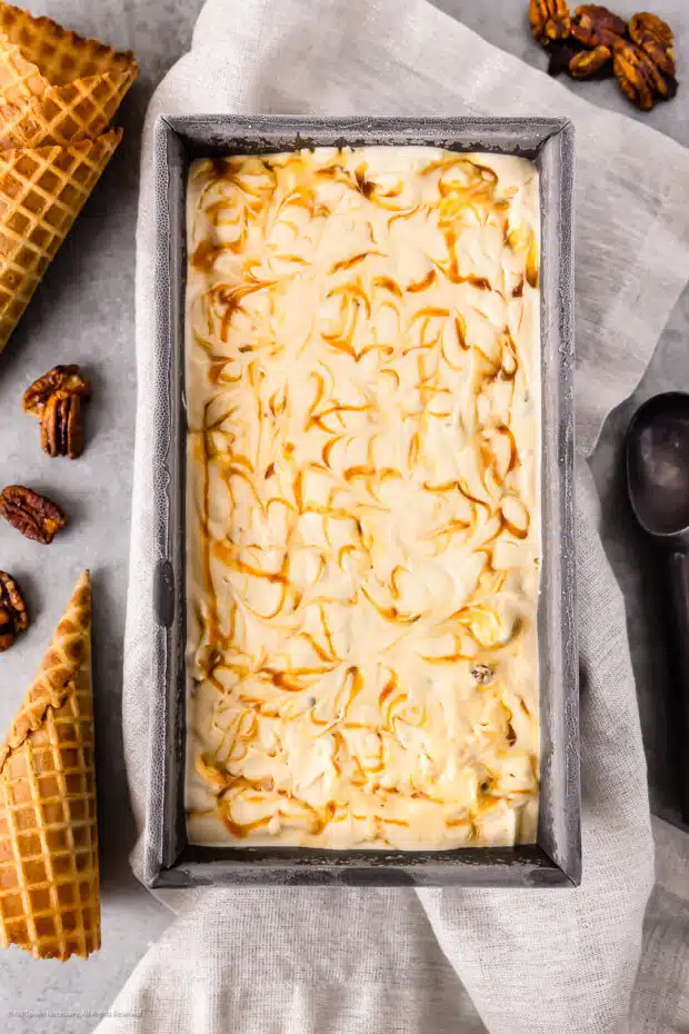 Overhead photo of butter pecan ice cream in a loaf pan with waffle cones next to the pan.