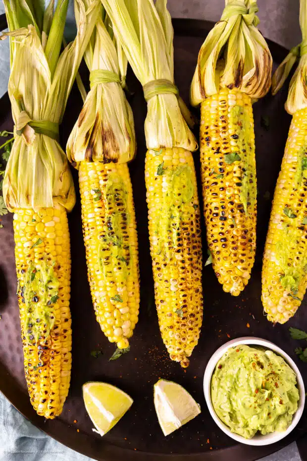 Overhead photo of five cobs of grilled corn slathered with avocado butter spread.