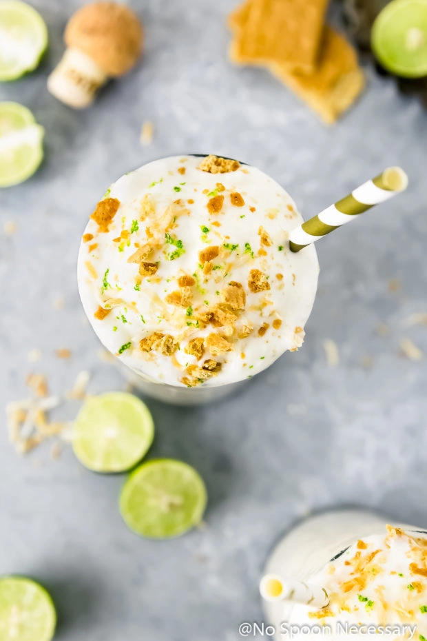 Overhead shot of a Lime Milkshake topped with whipped cream, crushed graham crackers and lime zest with halved key limes and graham crackers surrounding the glass.