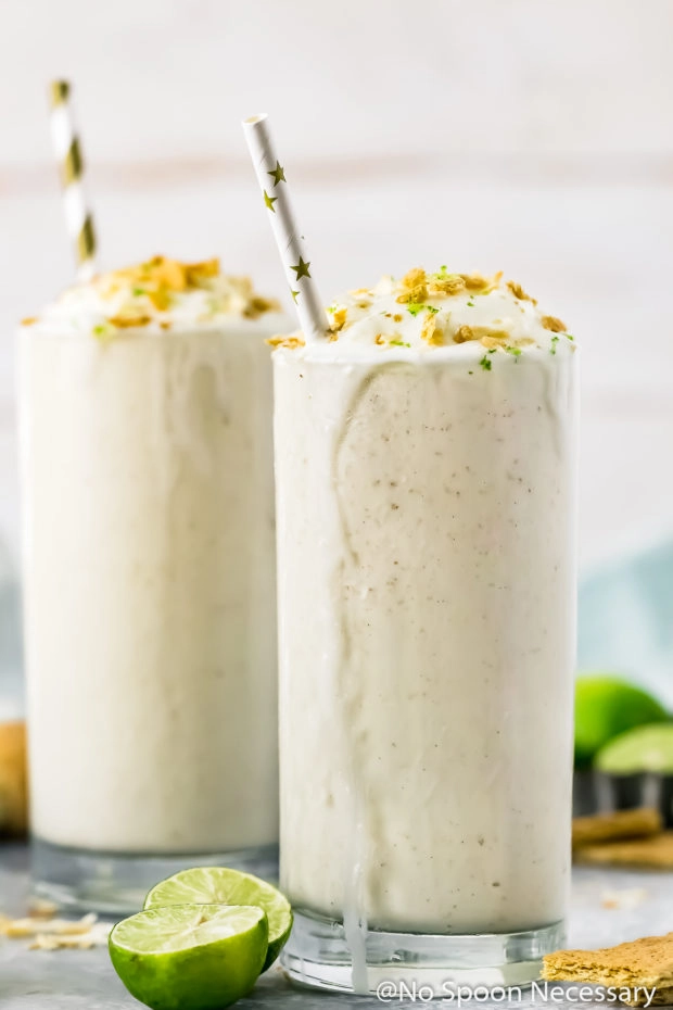 Straight on shot of two melting Lime Milkshakes topped with whipped cream, crushed graham crackers and lime zest. 