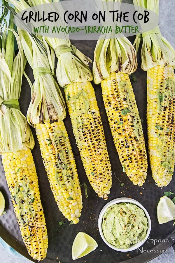 Overhead shot of Grilled Corn with Avocado Sriracha Butter on a black platter with lime wedges and fresh cilantro; and the words "Grilled Corn on the Cob with Avocado-Sriracha Butter" written on the photo.