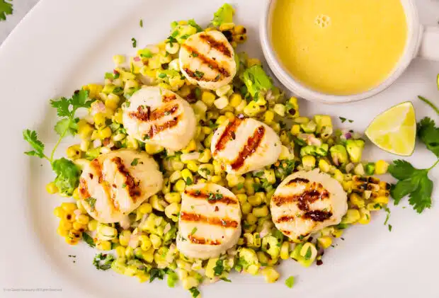 Photo of grilled scallops with corn and avocado salsa on a white platter.