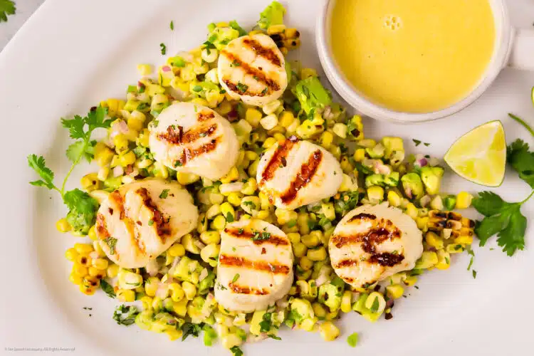 Photo of grilled scallops with corn and avocado salsa on a white platter.