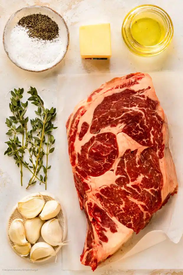 Overhead photo of the ingredients for slow cooking a steak in the oven neatly arranged on white counter.