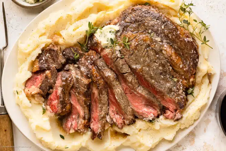 Overhead photo of perfectly slow cooked steak from the oven on a bed of mashed potatoes.