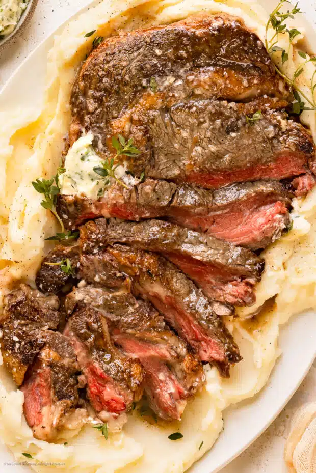 Photo of thinly sliced slow cooked ribeye on a fluffy mashed potatoes.