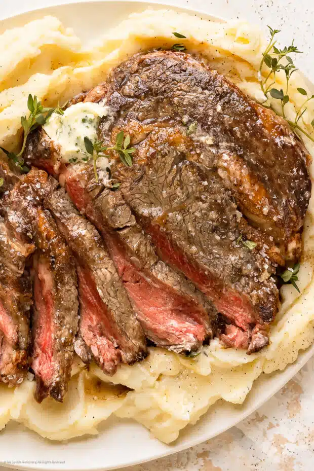 Overhead photo of thinly sliced slow cooked ribeye steak on a bed of mashed potatoes.