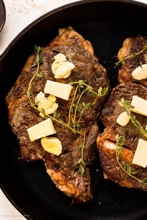 Overhead photo of a slow oven cooked rib eye steak topped with pats of butter and fresh thyme sprigs.