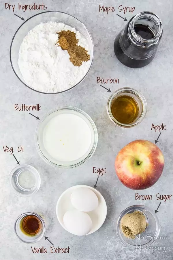 Overhead shot of the ingredients to make Apple Cinnamon Waffles with Bourbon Maple Syrup neatly organized on a gray surface.