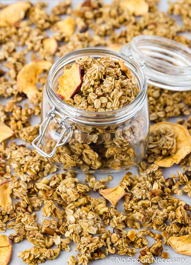 Angled shot of a clear mason jar full of Cinnamon Apple Pie Granola with more granola surrounding the jar