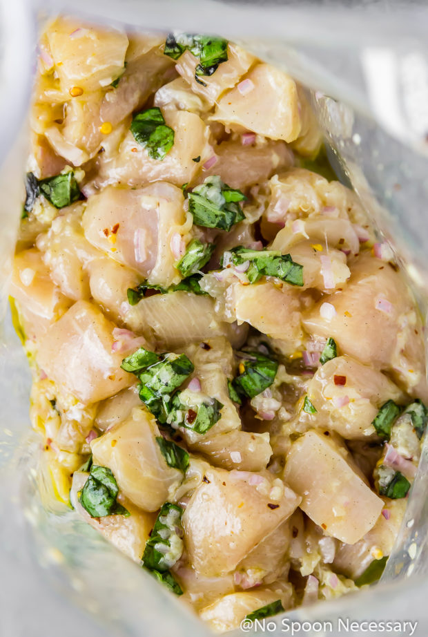 Overhead, close-up photo of cubed chicken tossed in a basil garlic marinade in a large resealable bag. (Process photo of step 1 of the recipe)