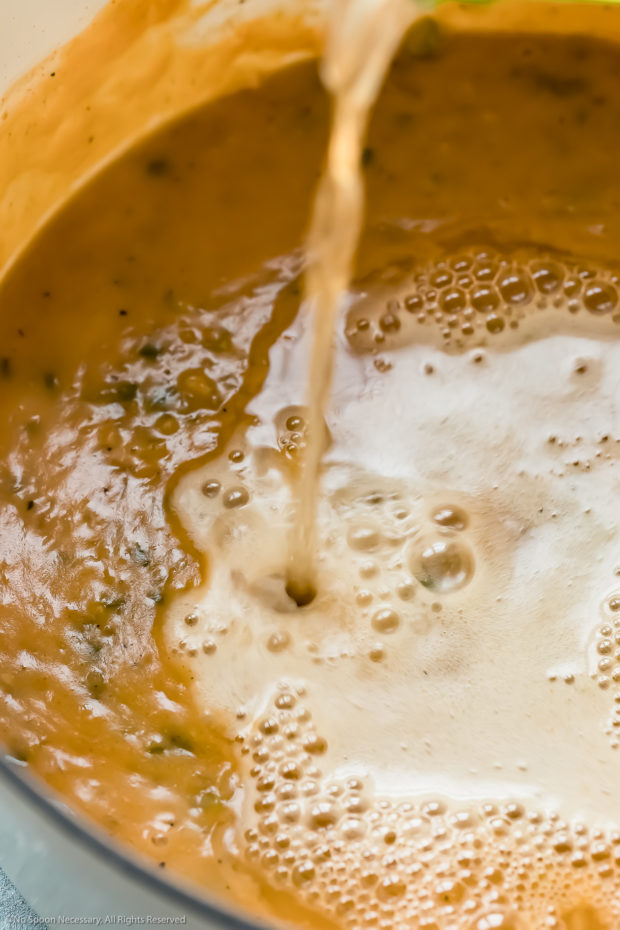 Angled photo of beer being poured into a soup - photo of step three in beer cheese soup recipe.