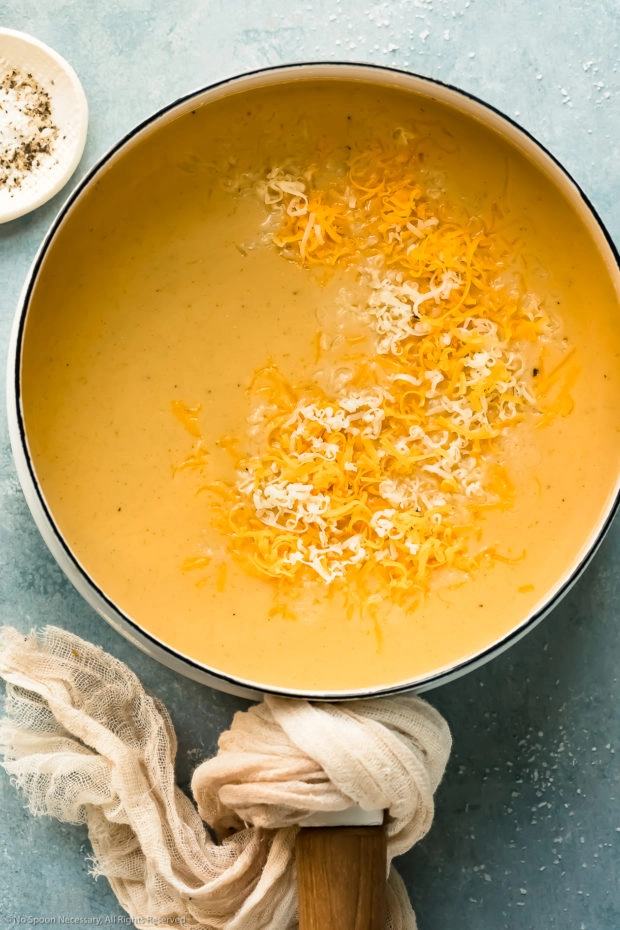 Overhead photo of a white saucepan filled with beer cheese soup and topped with shredded cheese before being stirred together - photo of step 5 of the recipe.