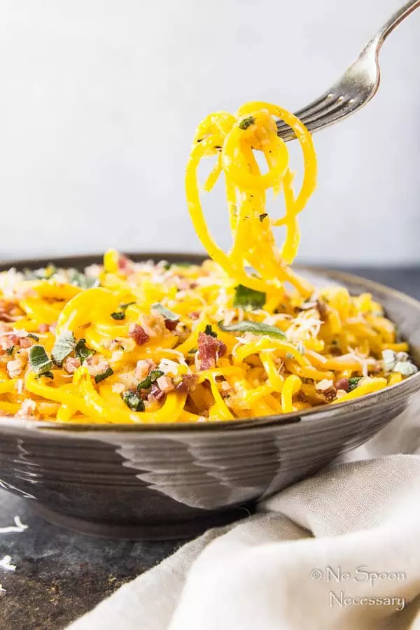 Straight on shot of Butternut Squash Noodle Carbonara in a brown serving bowl with a fork lifting some of the squash pasta carbonara up into the air.