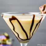 Straight on, up close shot of a Snickers Martini garnished with chocolate syrup and a mini snickers.