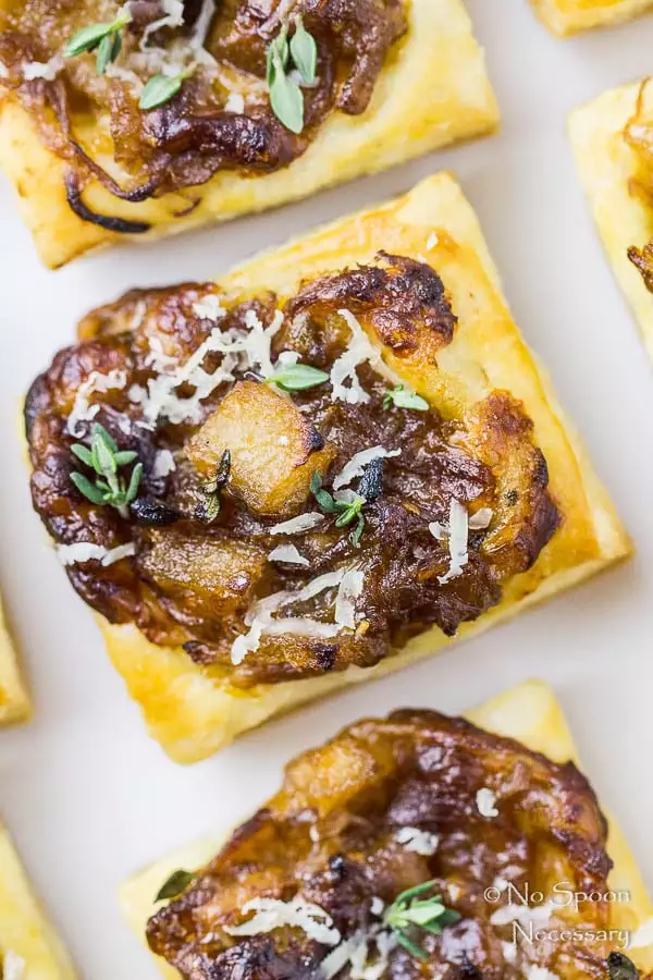 Overhead, up close shot of a white platter filled with Caramelized Onion Pear Tarts with the focus on one individual puff pastry tart.