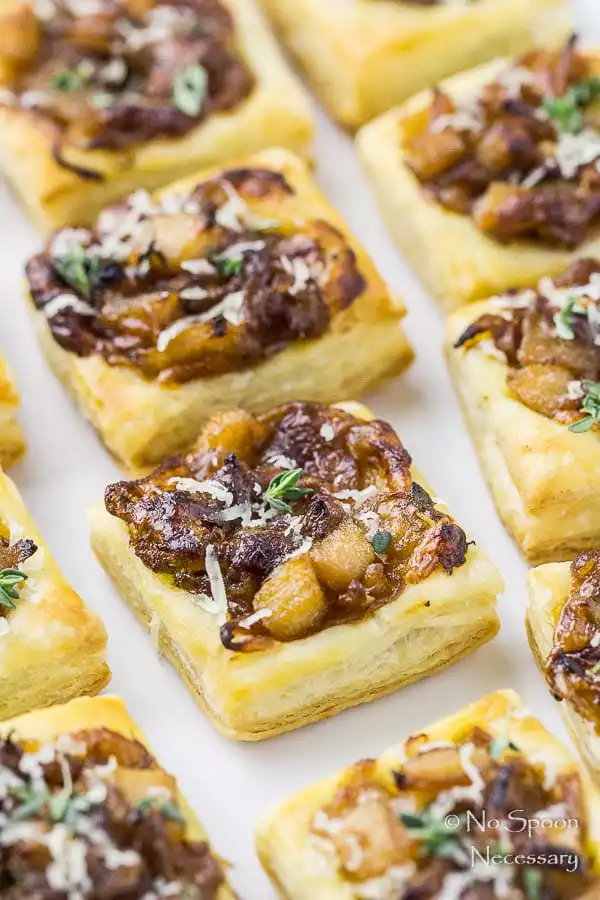 Angled, up close shot of a white platter filled with Caramelized Onion Pear Tarts garnished with fresh thyme with the focus on one individual tart.